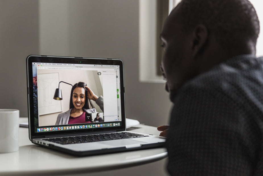 A shot of a video conference with a woman who can be seen smiling on screen. A man is sitting in front of the computer.